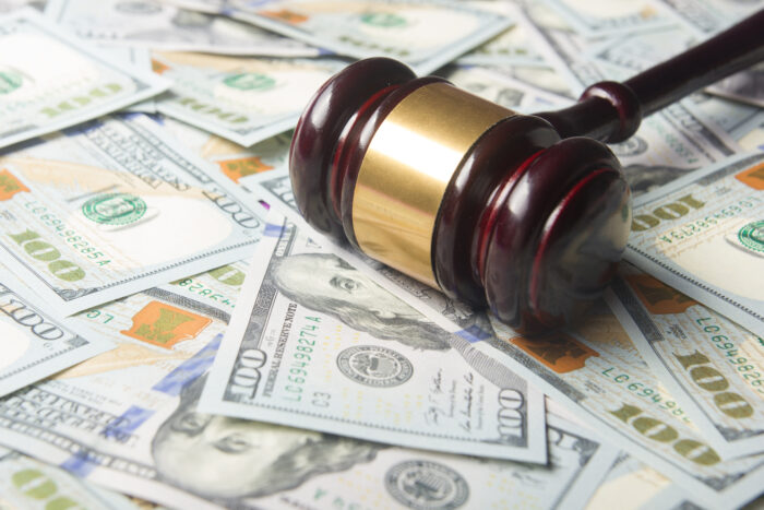 A brown wooden gavel sits on top of a pile of new one-hundred-dollar bills.