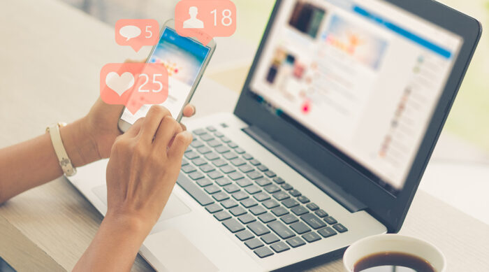 Woman reads comments and social media likes on her smartphone and laptop computer.