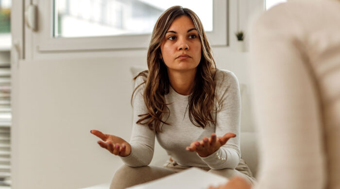 A woman sits with a lawyer and holds her hands out during a discussion.